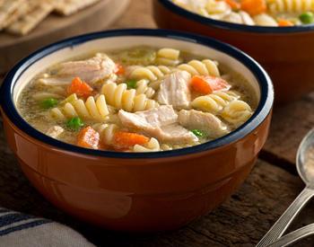 A bowl of chicken noodle soup with peas, carrots, and celery.