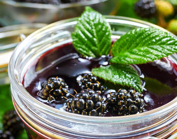 A jar of blackberry jam with mint leaves placed on top for garnish.