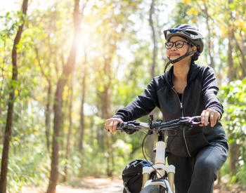 A middle-aged woman biking in a forest.