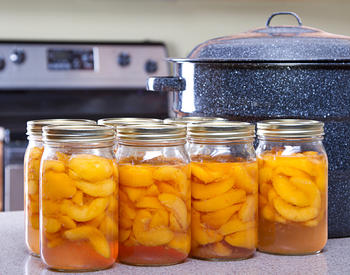 Peaches in mason jars with two-piece lids and a large pot behind them.