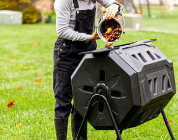 A gardener dumping compost into a rotating composter.