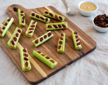 A cutting board with sliced celery topped with peanut butter and raisins.