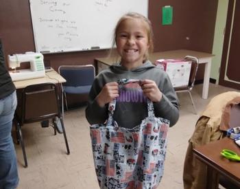 A girl smiles as she holds a tote bag she created for a military veteran.