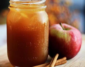 A mason jar of apple cider with an apple and cinnamon sticks next to it as garnish.