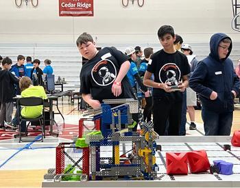 Disconauts teammates direct their robot to dump green blocks into the collection bin, scoring points.
