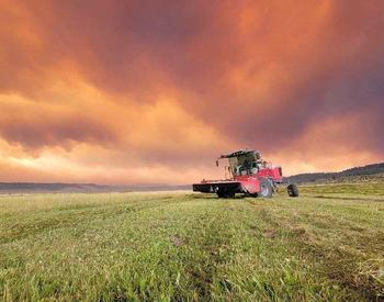 Photo of farm equipment in field with wildfire and smoky sky in background