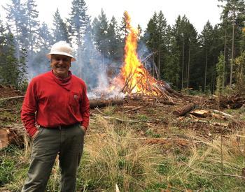Man in hard hat with a burning pile of debris in forest setting