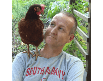 person in garden smiling at chicken on their shoulder